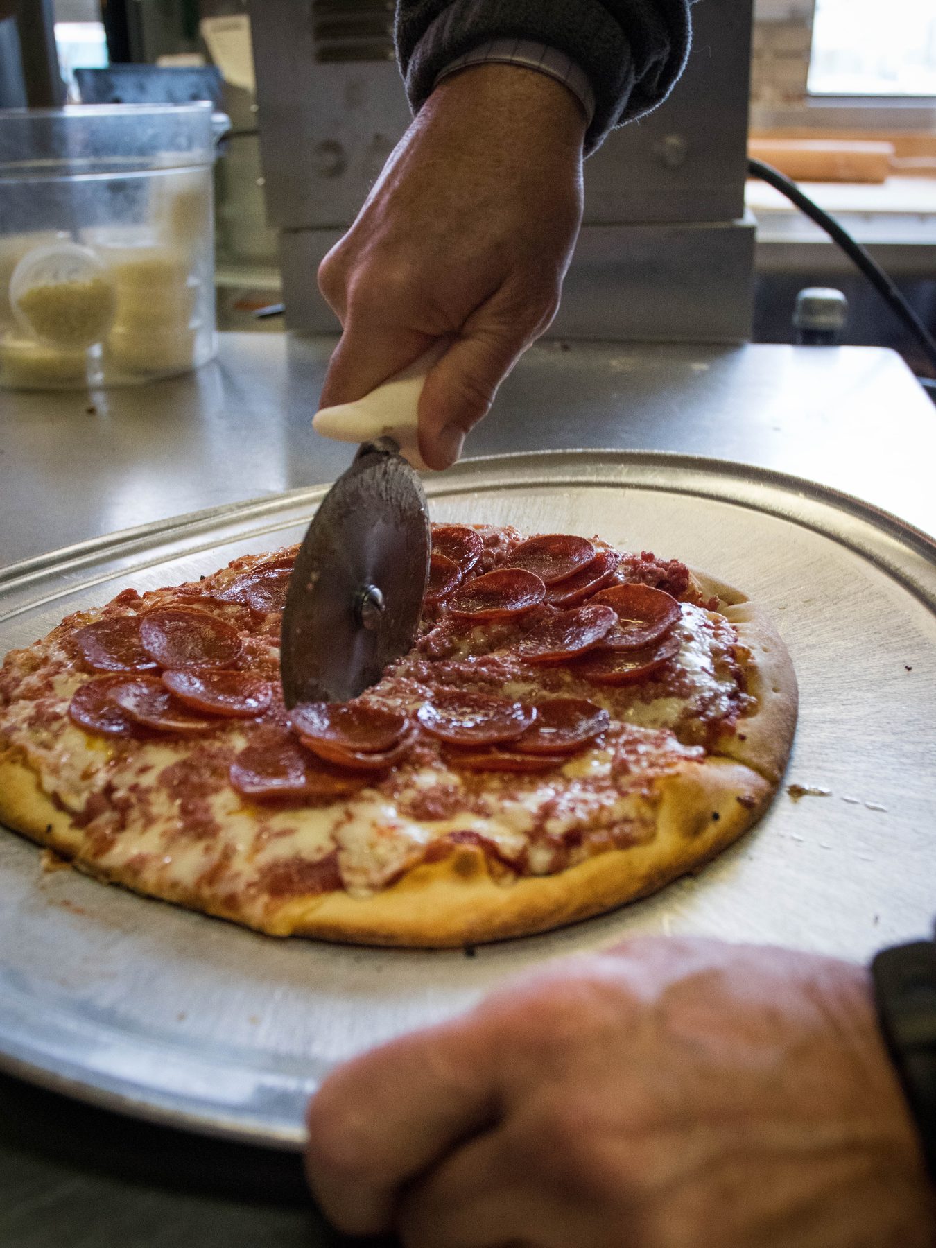 Cutting a fresh pepperoni pizza with a wheel cutter