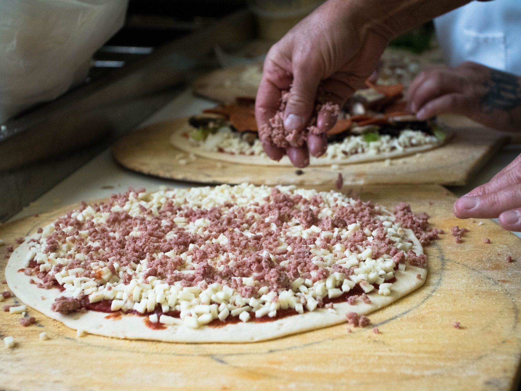 Hand-spreading sausage over cheese on a thin crust